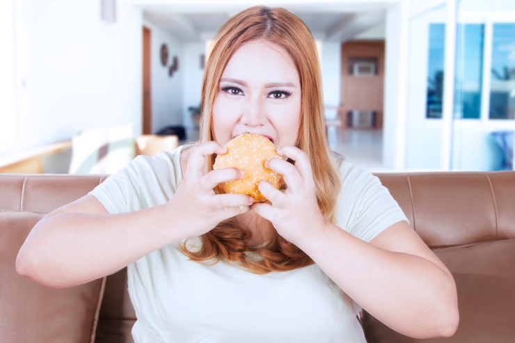 Beautiful blonde woman enjoy burger on sofa